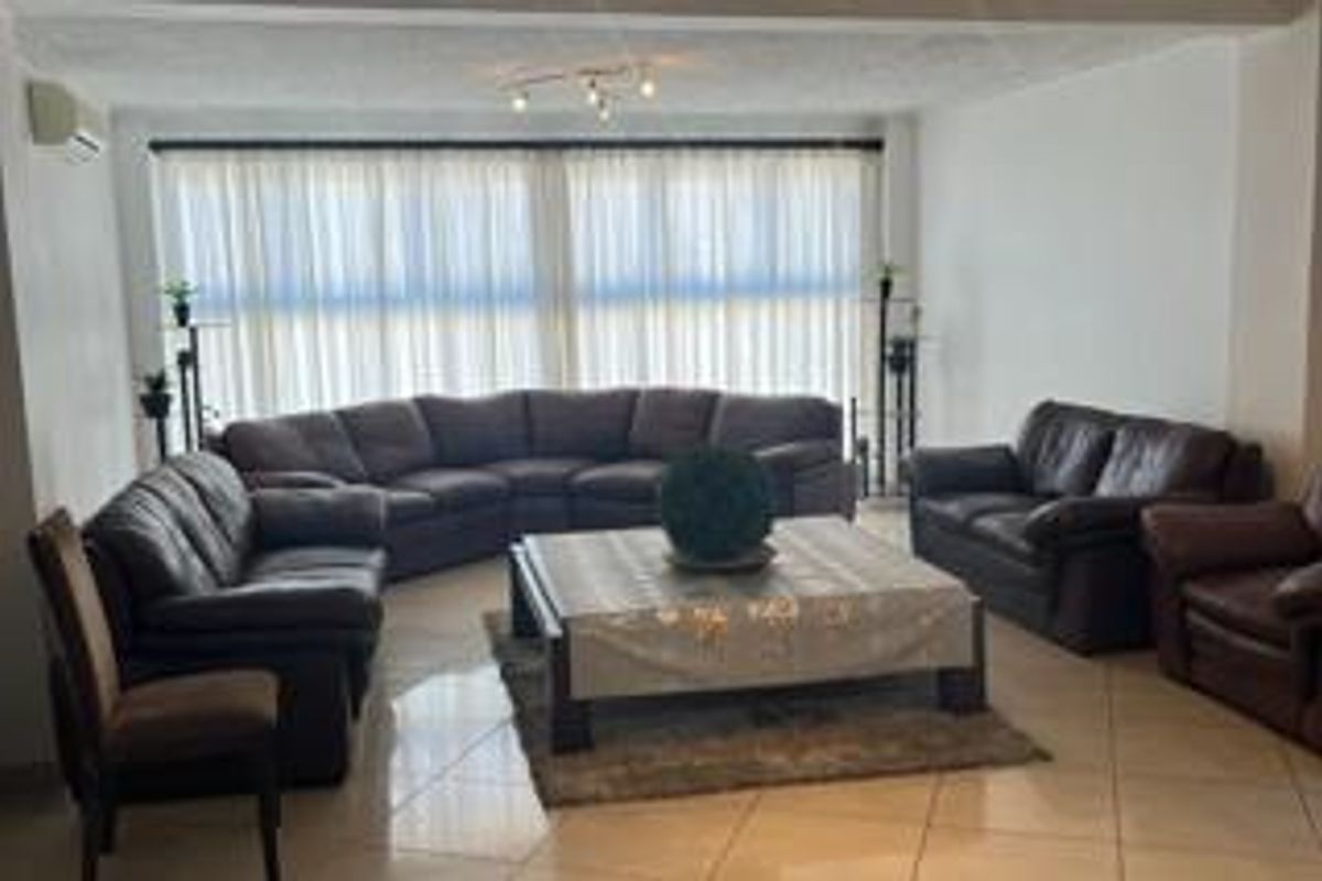 Spacious living room featuring large windows with sheer curtains, tiled flooring, and a neutral color palette, providing a comfortable and bright living space.