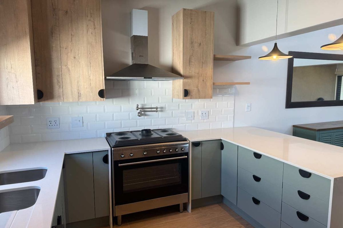 Modern kitchen featuring light wood-grain cabinetry, sage green base units, white quartz countertops, subway tile backsplash, and a stainless steel gas range with extractor.