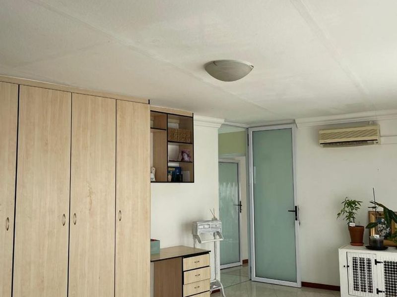 A bedroom featuring built-in wooden wardrobes, tiled flooring, an air conditioning unit, and a frosted glass door leading to an adjacent space.