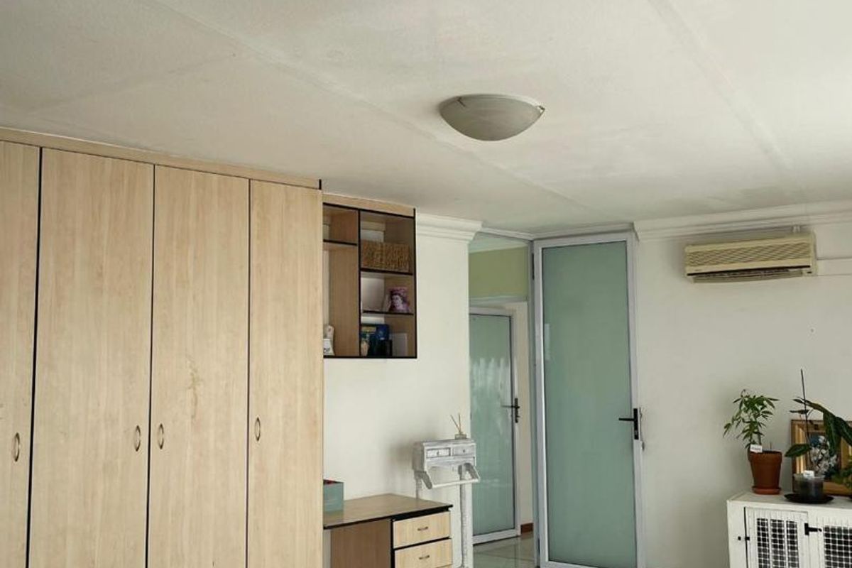A bedroom featuring built-in wooden wardrobes, tiled flooring, an air conditioning unit, and a frosted glass door leading to an adjacent space.