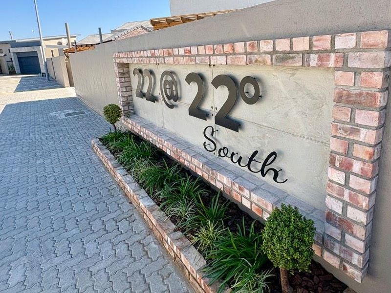 Front entrance view of the townhouse complex featuring a modern brick signage wall, paved driveway, and landscaped planter box.