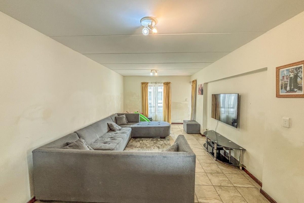 A spacious living room featuring tiled flooring and access to a balcony, requiring cosmetic updates to the walls and finishes.