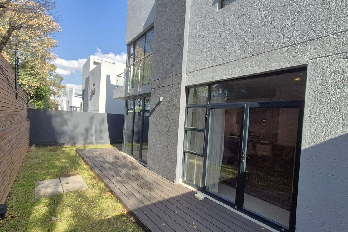 Rear view of a modern cluster home featuring a timber deck, large aluminium sliding doors, and a private garden with boundary walling.