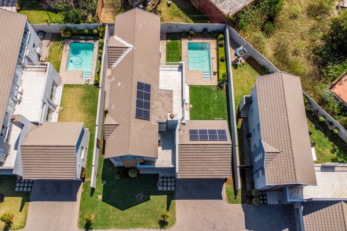 Aerial view of a residential property complex featuring multiple homes with tiled roofs, solar panels, private swimming pools, and paved driveways.