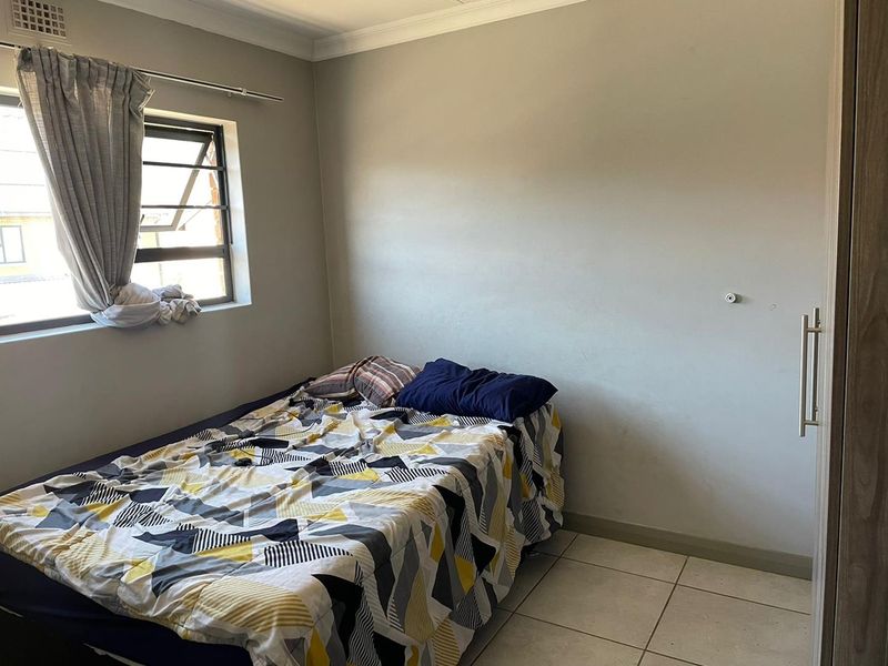 A functional bedroom featuring tiled flooring, a built-in wardrobe, and a louvered window providing natural light.