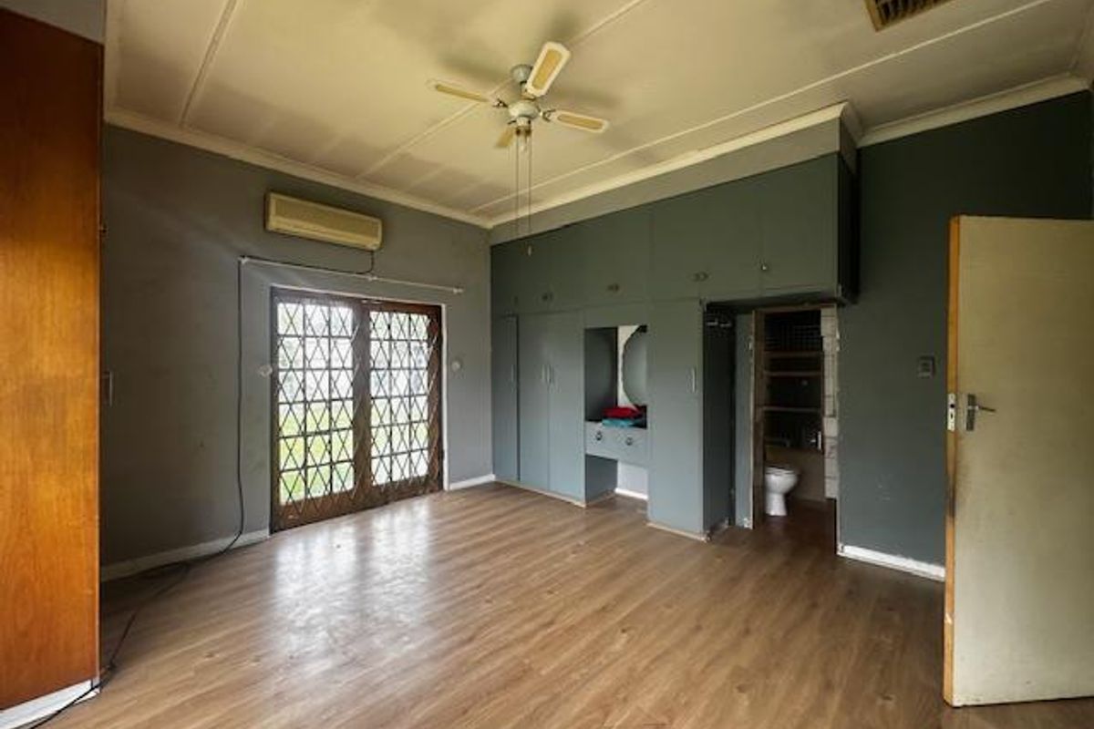 Spacious bedroom featuring built-in cupboards, laminate flooring, a ceiling fan, and an integrated air conditioning unit with direct access to an en-suite bathroom.