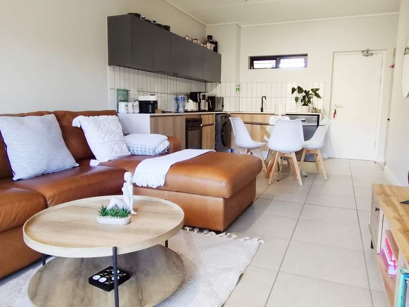 An open-plan living and kitchen area featuring modern cabinetry, tiled flooring, and a functional kitchen layout with integrated appliances.