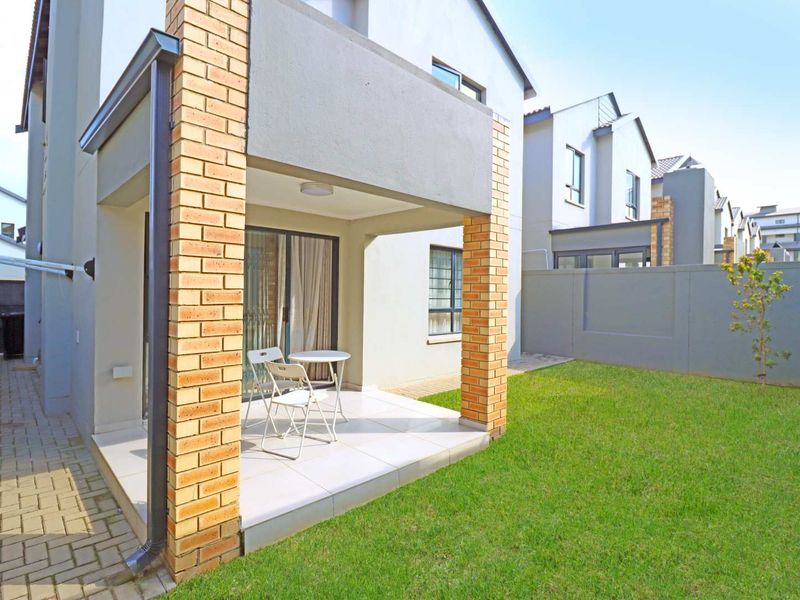 A covered patio area with tiled flooring and brick pillars, leading out to a private garden with a boundary wall.