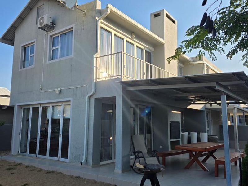 Rear view of a two-story house featuring a covered patio, balcony, and sliding glass doors, with visible wear on the exterior wall finish.