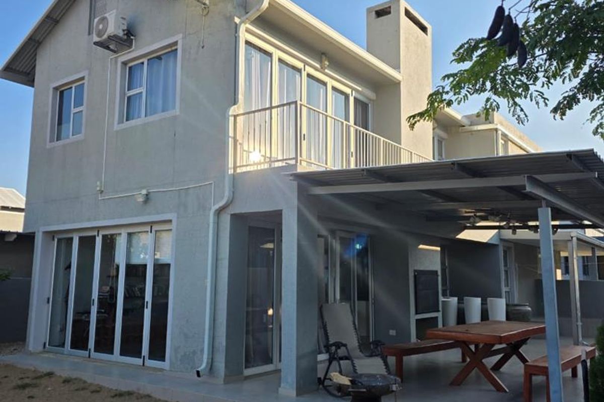 Rear view of a two-story house featuring a covered patio, balcony, and sliding glass doors, with visible wear on the exterior wall finish.