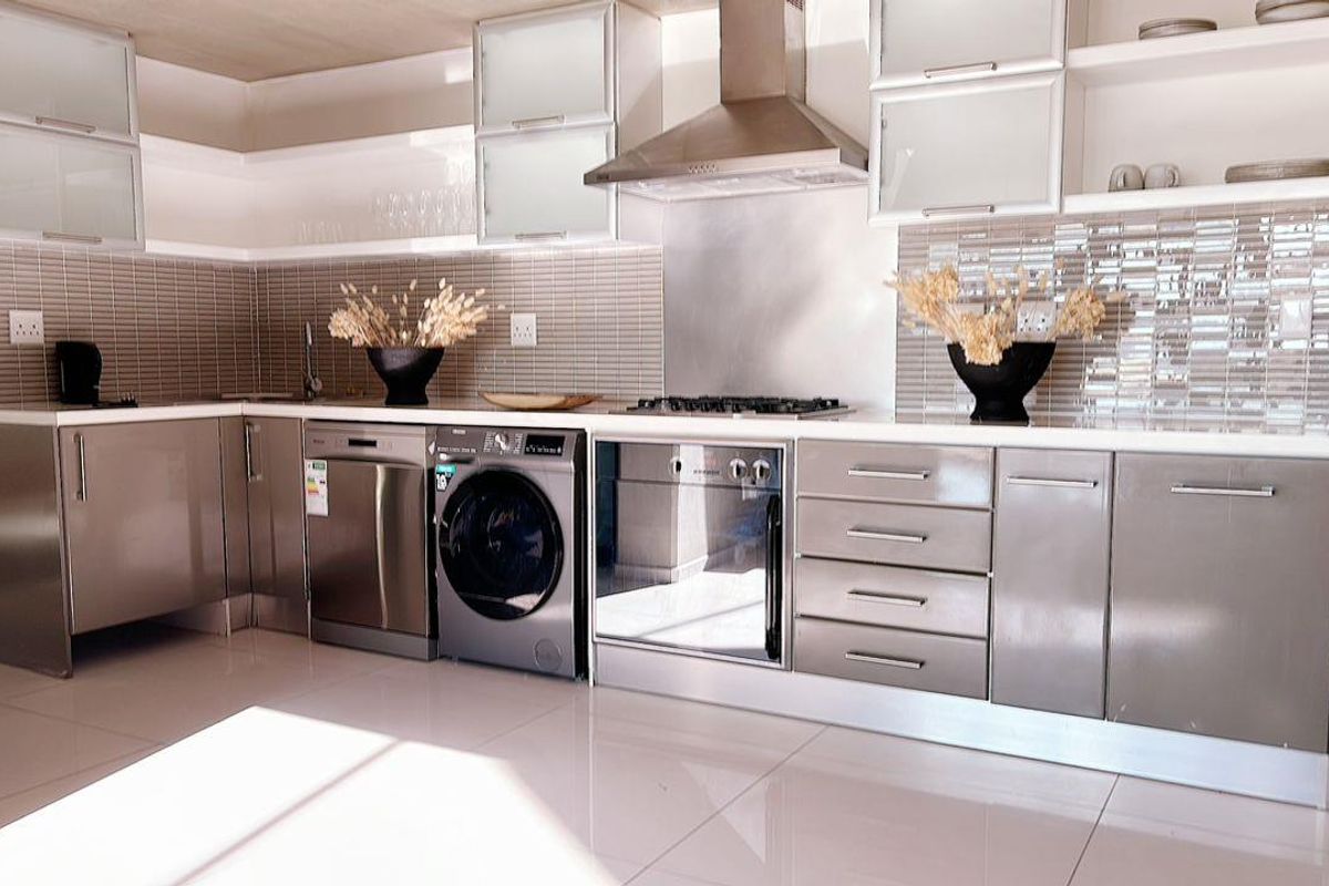 Modern kitchen featuring sleek metallic cabinetry, integrated stainless steel appliances, a gas hob with extractor fan, and tiled backsplash.