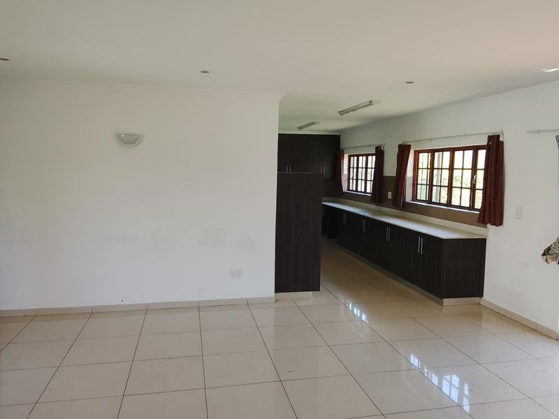 An open-plan living and kitchen area featuring tiled flooring, dark built-in cabinetry, and large windows providing natural light.