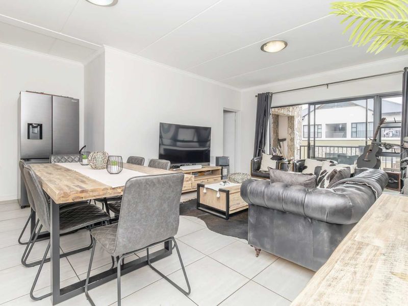 An open-plan living and dining area featuring tiled flooring, neutral walls, and a large sliding glass door leading to a balcony.