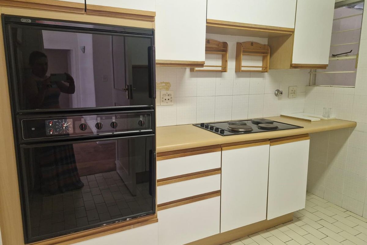 A functional kitchen featuring built-in cabinetry, a wall-mounted oven, and a four-plate electric hob with tiled splashbacks and flooring.
