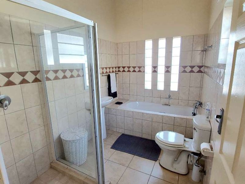 A functional bathroom featuring a glass shower enclosure, built-in bathtub, pedestal basin, and toilet, finished with tiled surfaces and exposed timber ceiling beams.