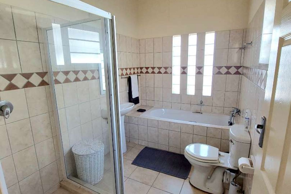 A functional bathroom featuring a glass shower enclosure, built-in bathtub, pedestal basin, and toilet, finished with tiled surfaces and exposed timber ceiling beams.