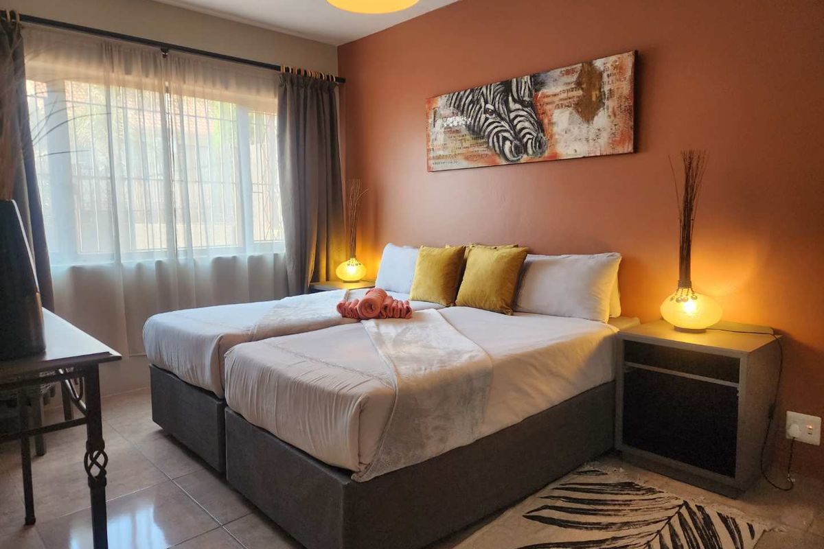 A well-lit bedroom featuring tiled flooring, a large window with curtain tracks, and a warm-toned accent wall.