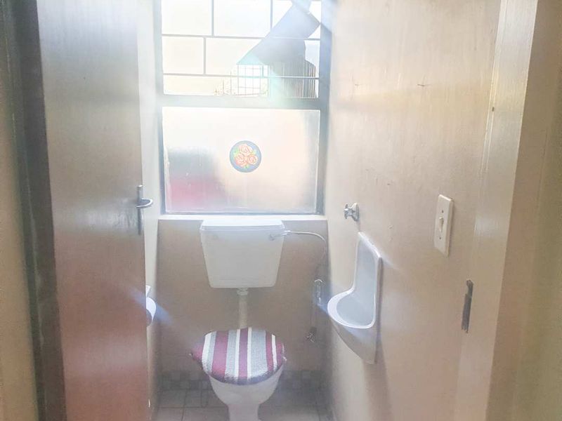 A compact bathroom featuring a toilet, a wall-mounted urinal, and a window with security bars, requiring cosmetic updates to improve its overall condition.