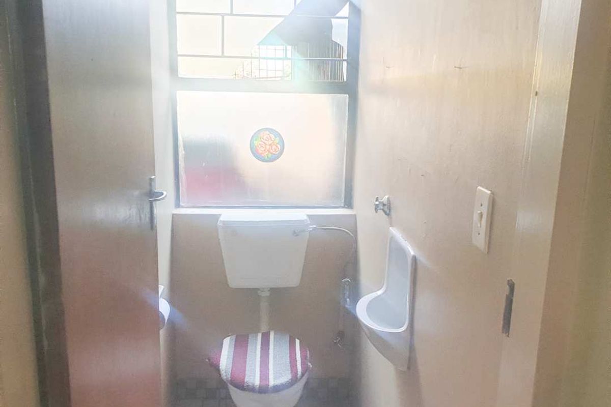A compact bathroom featuring a toilet, a wall-mounted urinal, and a window with security bars, requiring cosmetic updates to improve its overall condition.