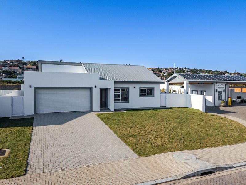 Modern single-story residential property featuring a clean white facade, corrugated metal roof, paved driveway, and integrated garage, situated in a well-maintained estate.