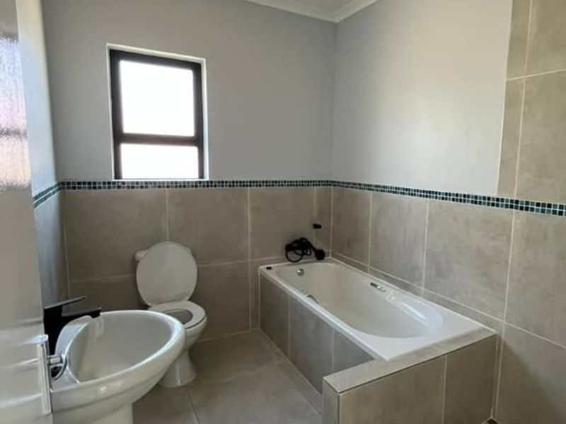 A clean, modern bathroom featuring a pedestal basin, toilet, built-in bathtub, and a separate tiled shower enclosure with neutral wall and floor tiling.