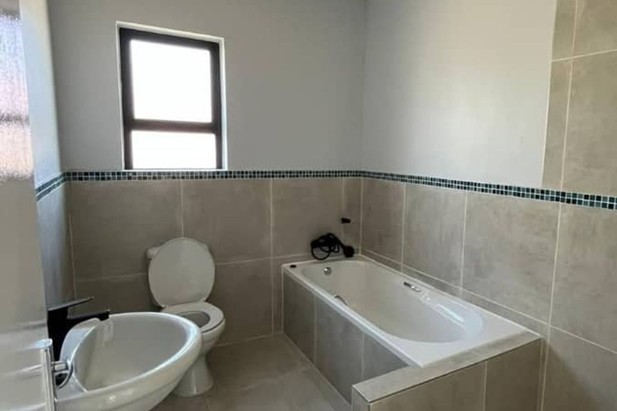 A clean, modern bathroom featuring a pedestal basin, toilet, built-in bathtub, and a separate tiled shower enclosure with neutral wall and floor tiling.