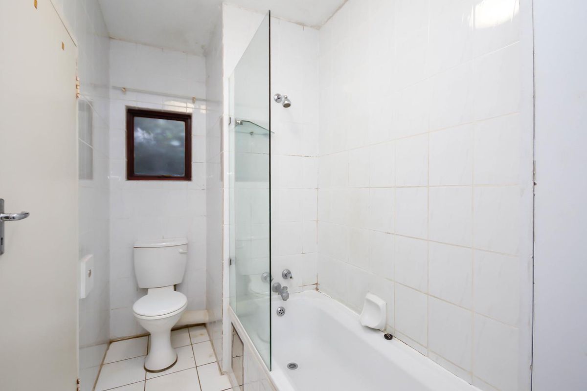 A functional bathroom featuring a white bathtub with a glass shower screen, a standard toilet, and fully tiled walls and flooring.