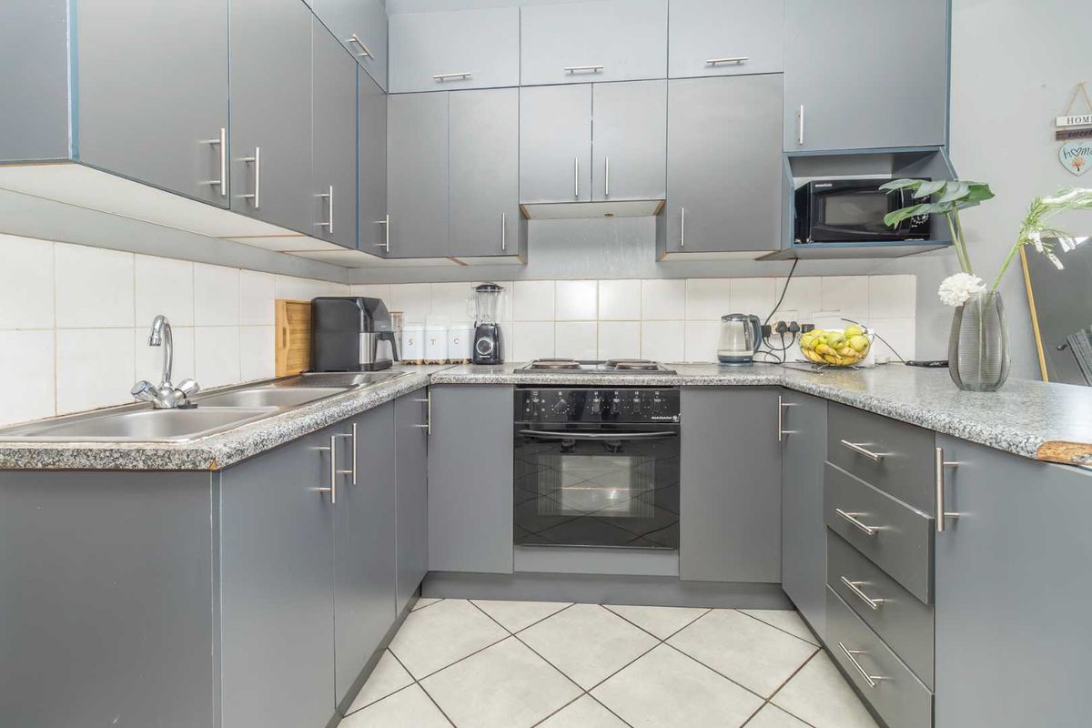 A functional U-shaped kitchen featuring grey cabinetry, laminate countertops, a built-in oven with hob, and tiled flooring.