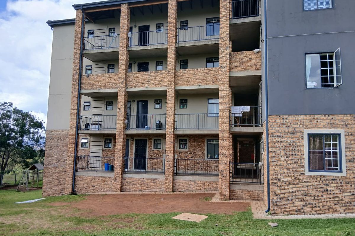 Exterior view of a multi-story apartment building featuring face brick facade, metal balcony railings, and paved ground level access.