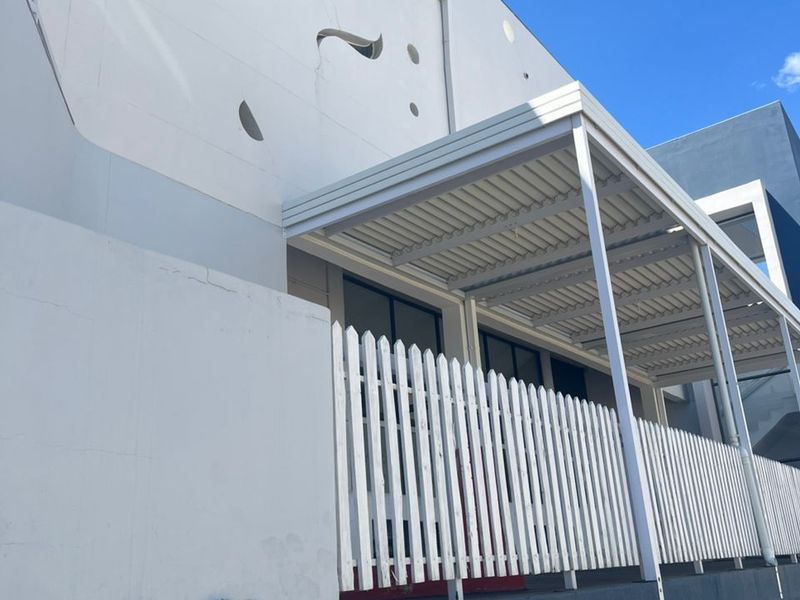 Exterior view of an office building featuring a covered patio area with a white picket fence and distinctive porthole windows.