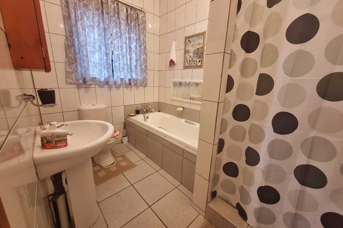 A functional bathroom featuring a pedestal basin, a built-in bathtub with tiled surround, and full-height wall tiling.