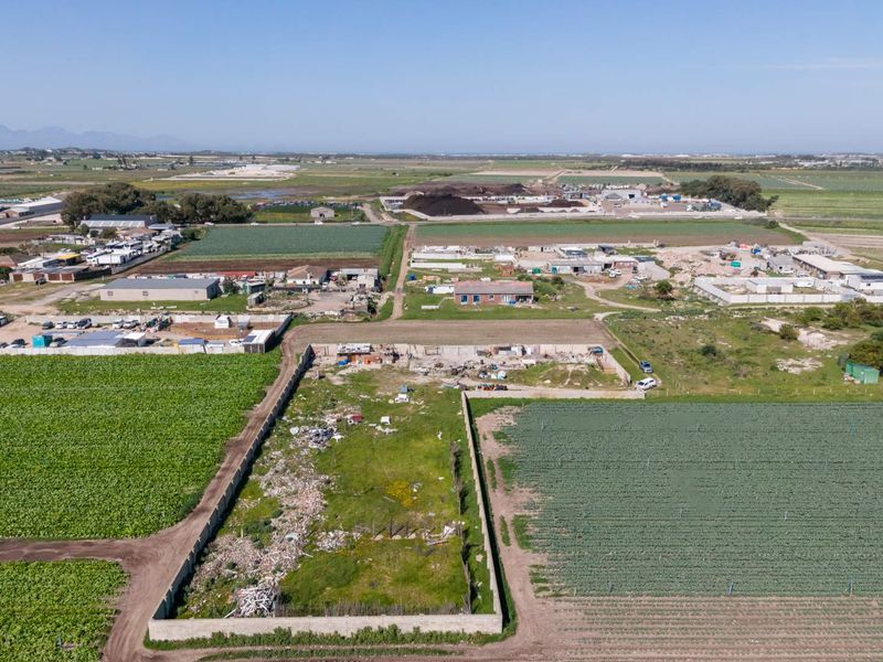 Aerial view of a vacant residential plot enclosed by perimeter walls, situated in a rural agricultural area.