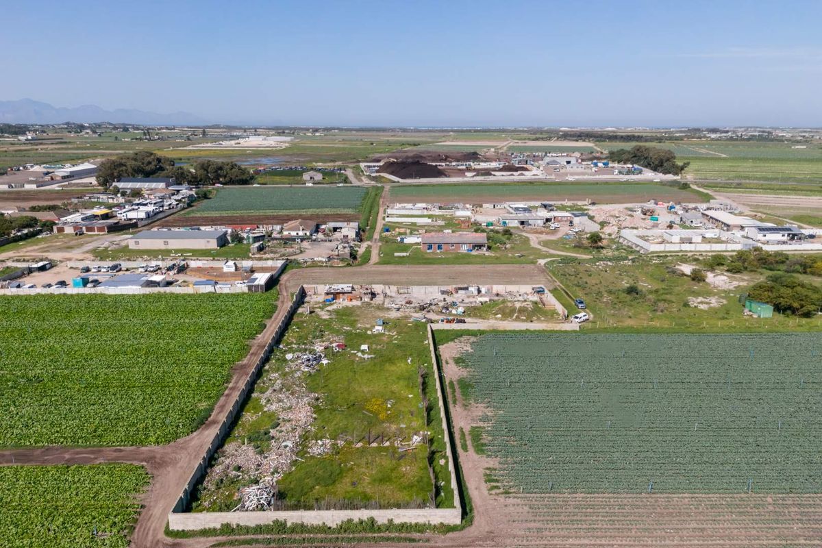 Aerial view of a vacant residential plot enclosed by perimeter walls, situated in a rural agricultural area.