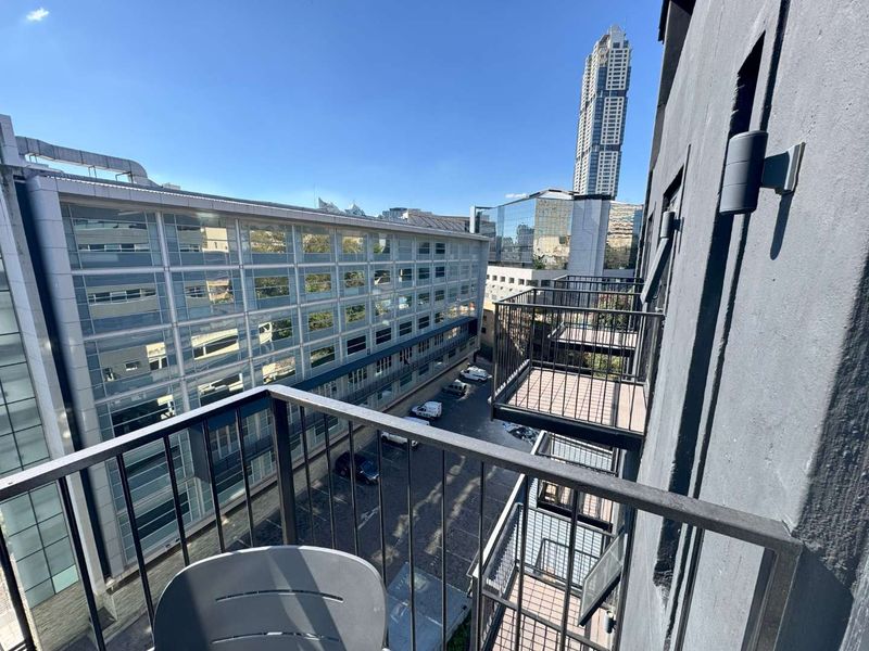 A modern apartment balcony featuring metal railings and decking, offering an elevated urban view of the surrounding city buildings.