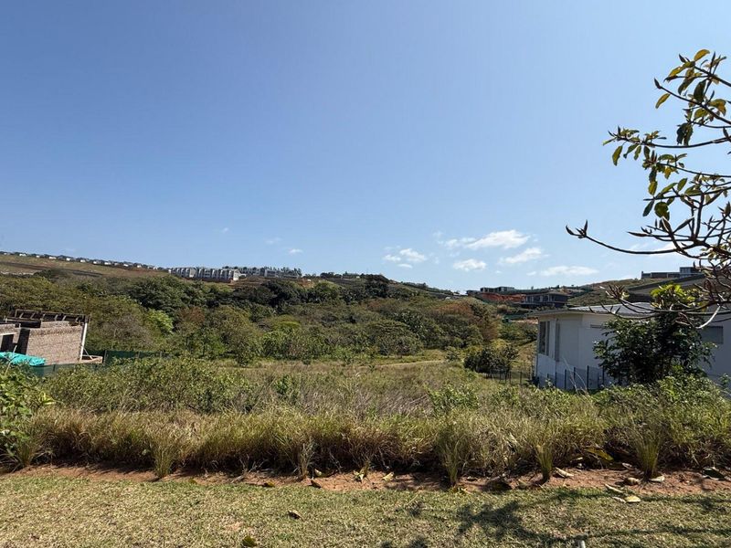 A wide-angle view of the vacant residential land, showcasing the natural landscape, surrounding vegetation, and distant hillside residential development.