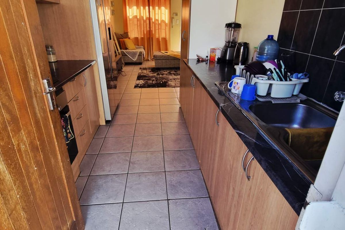 A functional galley-style kitchen featuring wood-look cabinetry, dark stone countertops, and tiled flooring, leading into an adjacent living area.