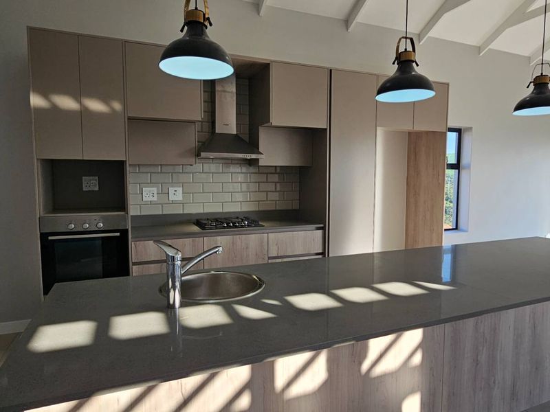 Modern kitchen featuring a large island with stone countertops, built-in oven, gas hob, and subway tile backsplash under a vaulted ceiling.