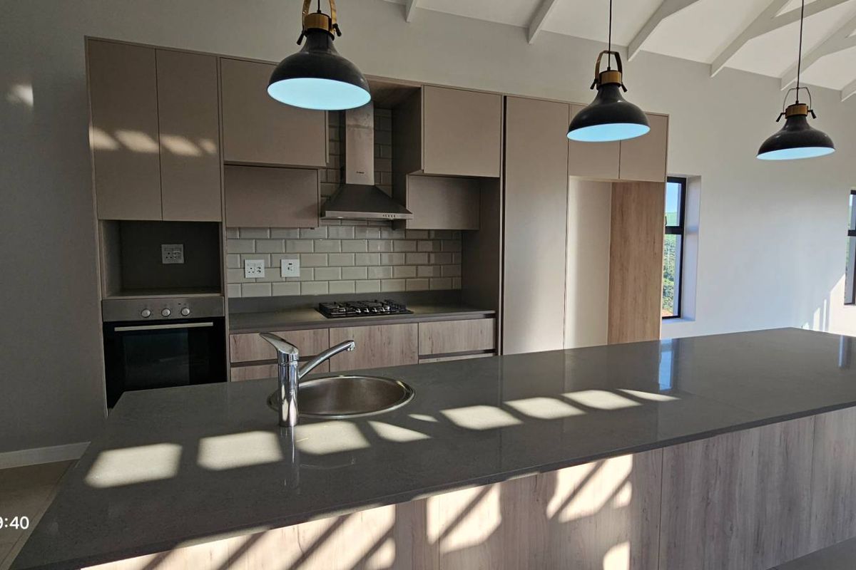 Modern kitchen featuring a large island with stone countertops, built-in oven, gas hob, and subway tile backsplash under a vaulted ceiling.