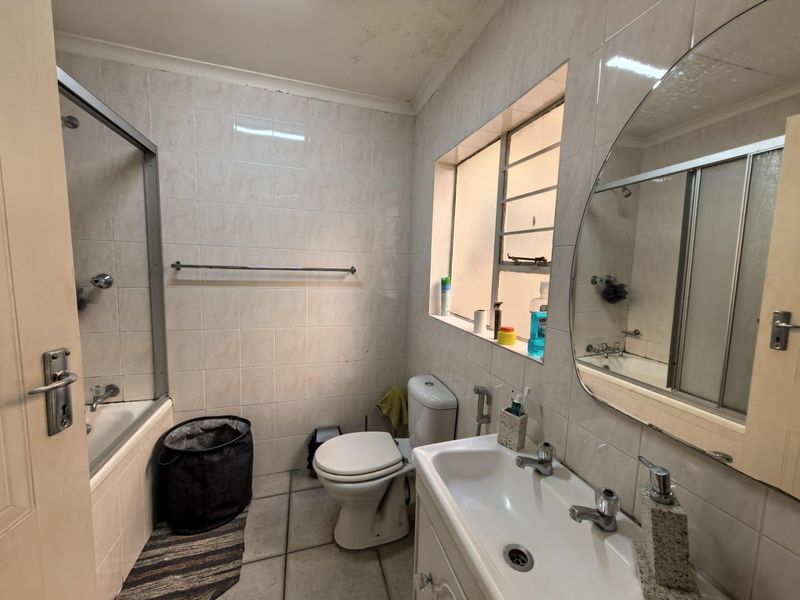 A functional bathroom featuring a bathtub with shower screen, vanity basin, and toilet, with tiled finishes throughout. Requires cosmetic updates and ceiling repairs.