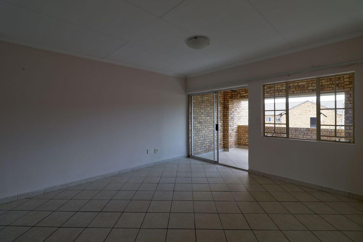 An empty, neutrally painted living room featuring tiled flooring, a sliding glass door leading to a balcony, and security bars on the windows.