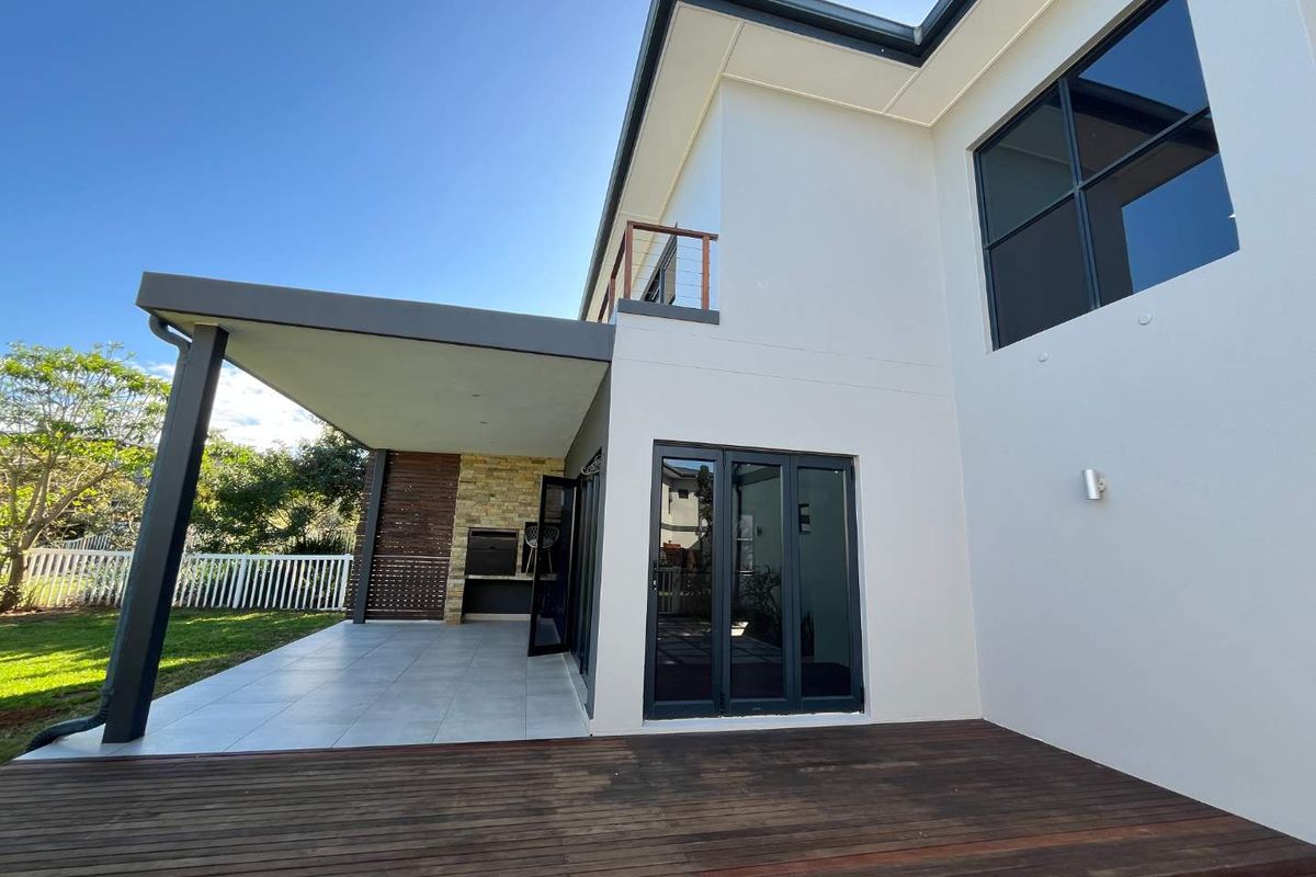Rear exterior view featuring a covered patio with built-in braai, timber decking, and modern bi-fold doors leading into the home.
