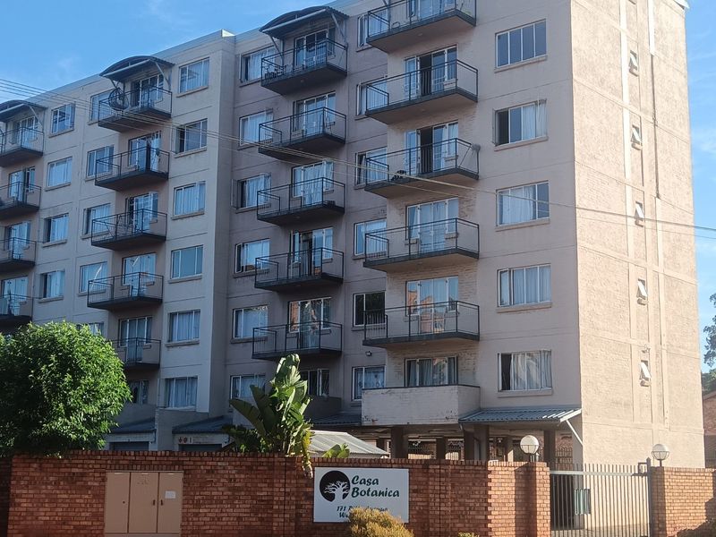 Exterior view of the Casa Botanica apartment complex, featuring multi-story residential units with private balconies and a secure brick boundary wall.