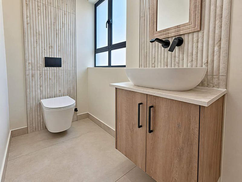Modern bathroom featuring a wall-mounted toilet, wood-finish vanity with vessel sink, matte black fixtures, and elegant textured wall tiling.