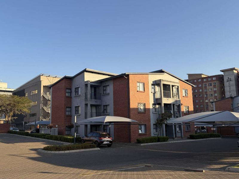 Exterior view of a multi-story apartment complex featuring brick and plaster facade, private balconies, and covered parking bays.