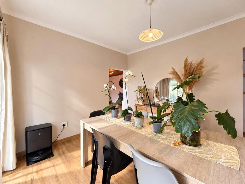 A bright dining room featuring light wood-look laminate flooring, neutral wall tones, and a modern pendant light fixture.
