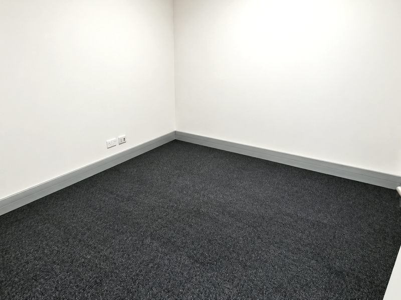 A clean, empty office space featuring neutral walls, dark grey carpeting, and integrated electrical outlets, ready for professional use.