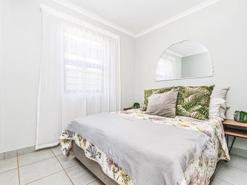 A bright and well-maintained bedroom featuring neutral tiled flooring, a window with security bars, and classic cove cornicing.
