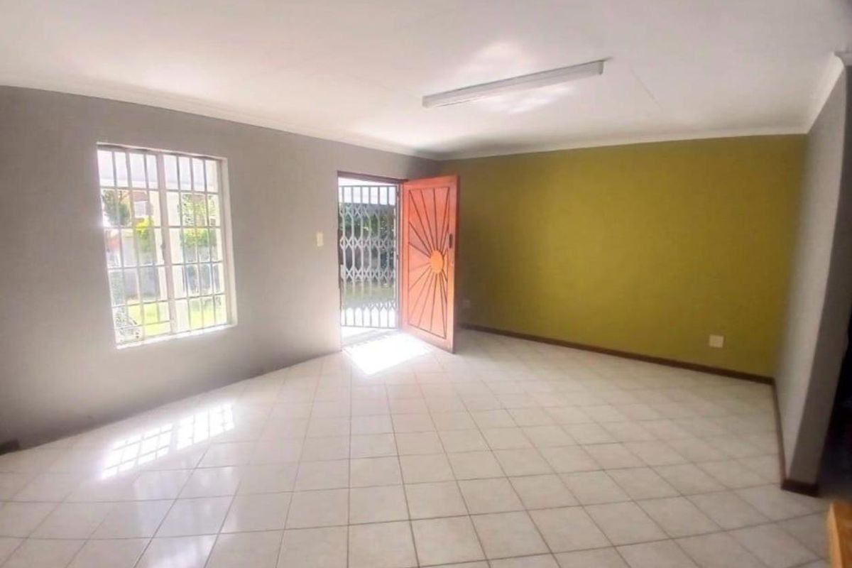 A bright, open-plan living area featuring tiled flooring, a security gate at the entrance, and large windows allowing for natural light.