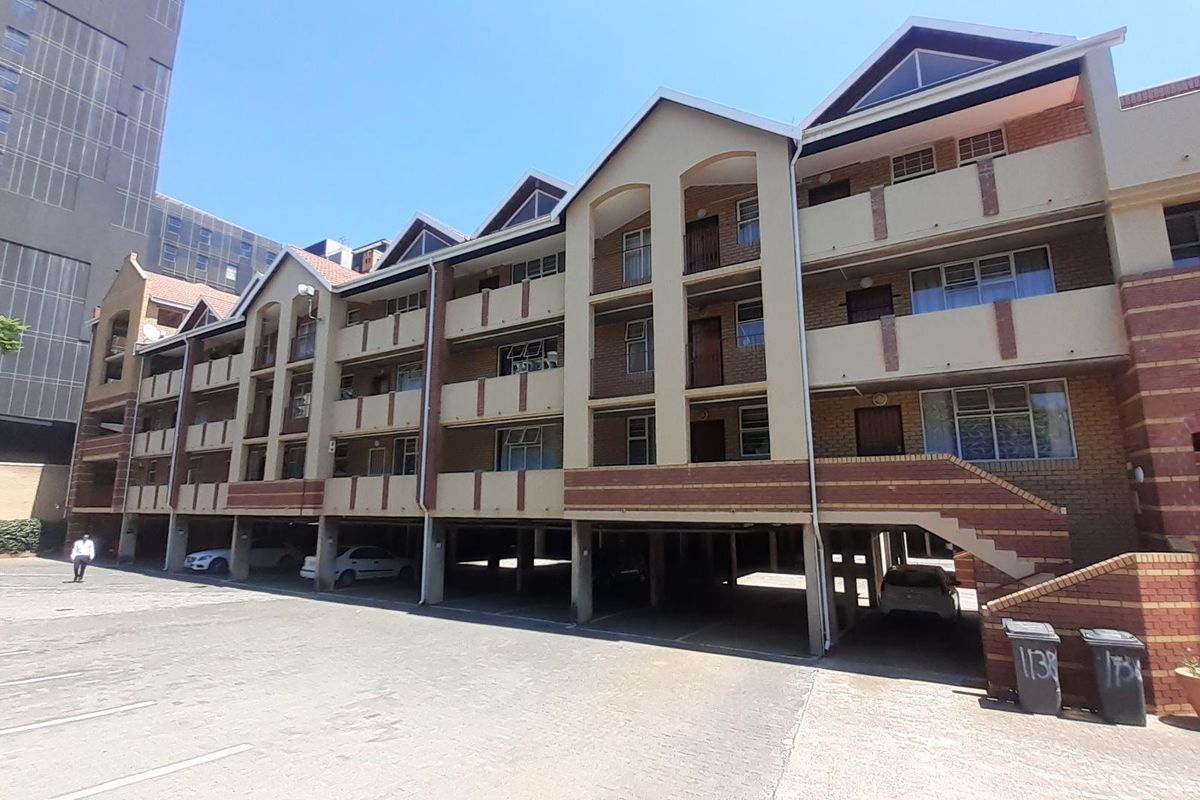 Exterior view of a multi-story apartment building featuring brick facade, balconies, and ground-level covered parking.