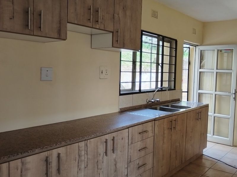 A functional kitchen featuring wood-look laminate cabinetry, durable countertops, a stainless steel sink, and tiled flooring with direct access to the exterior.